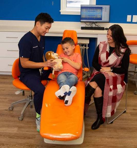 Dentist holds a stuffed animal while a child brushes the stuffed animals teeth during a pediatric dental appointment.